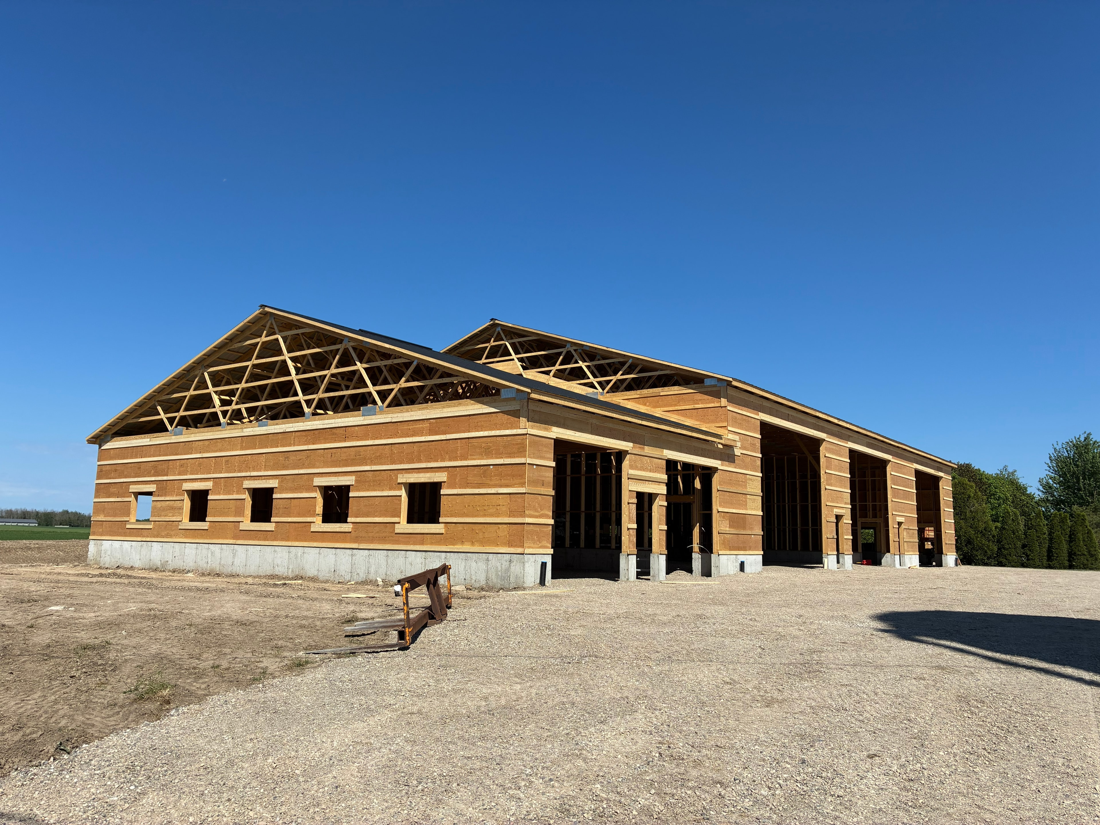 Large barn under construction with exposed wood frame trusses and open bays